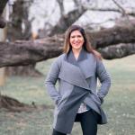 Photograph of Lauren, a white woman with long brown hair, standing in front of a tree wearing a grey coat.