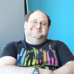 Moshe sitting down, head slightly to the side. His t-shirt has Guardians of the Galaxy silhoutes against a background of sound visualization bars.